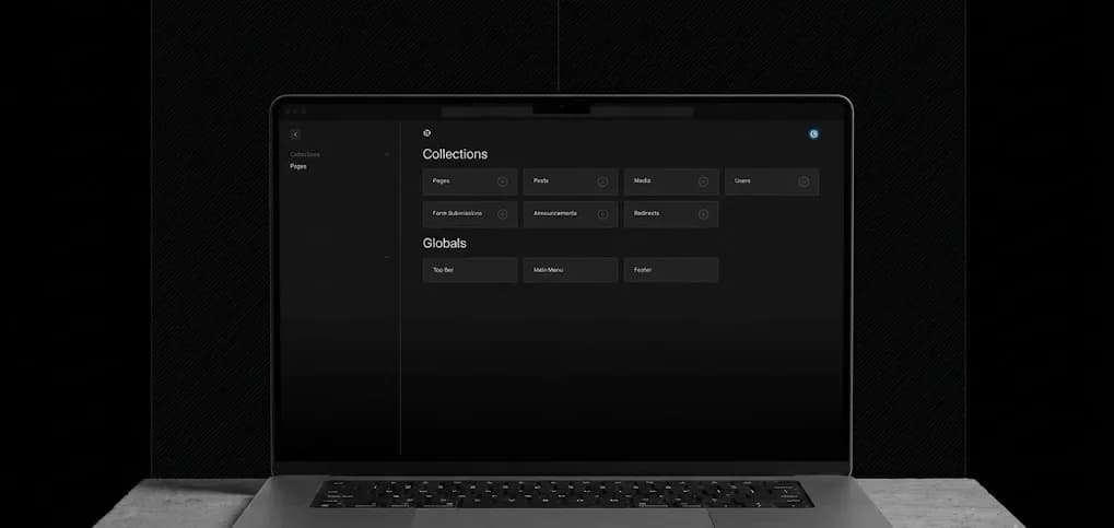 A front-facing dark gray laptop resting on a concrete surface against a dark textured background, displaying a dark mode web CMS dashboard with Collections and Globals sections on its screen without any floating UI elements.